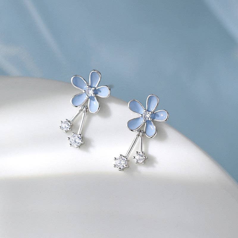 Flower-shaped earrings with blue petals and clear stones on a light gray background