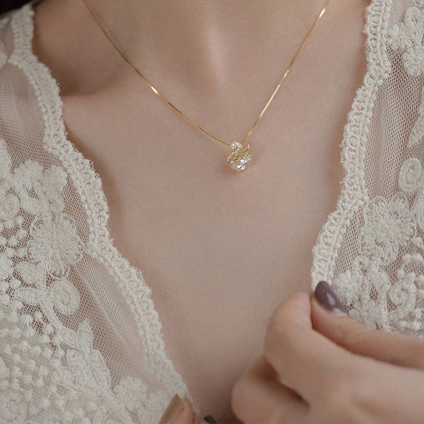 Close-up of a gold necklace with a swan-shaped pendant on a person wearing a lace garment.