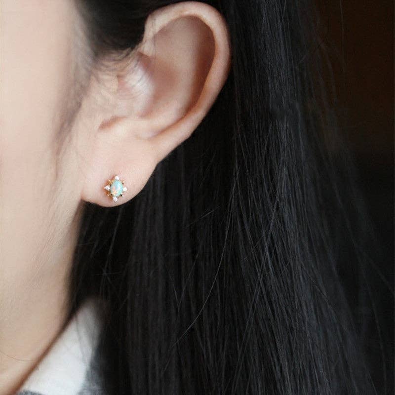 Close-up of an ear wearing a small opal stud earring with dark hair in the background.