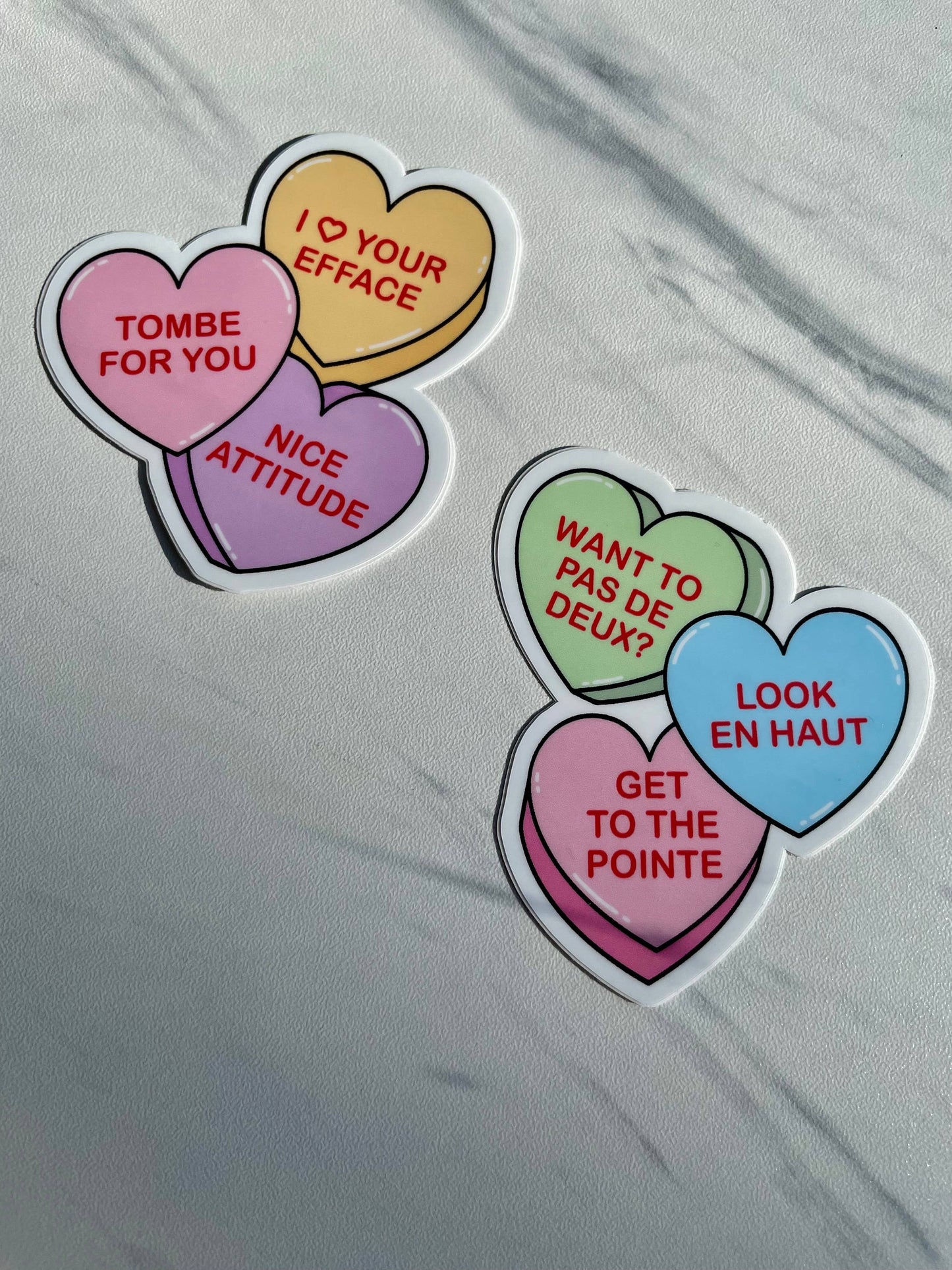 Heart-shaped stickers with French dance step phrases on a gray surface