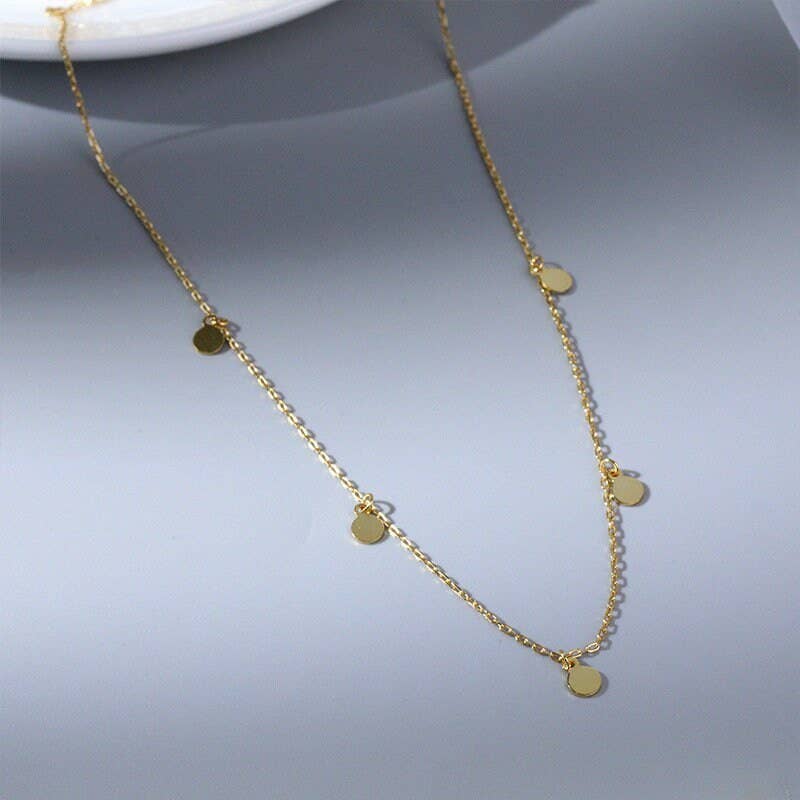 Gold necklace with small round pendants on a gray background