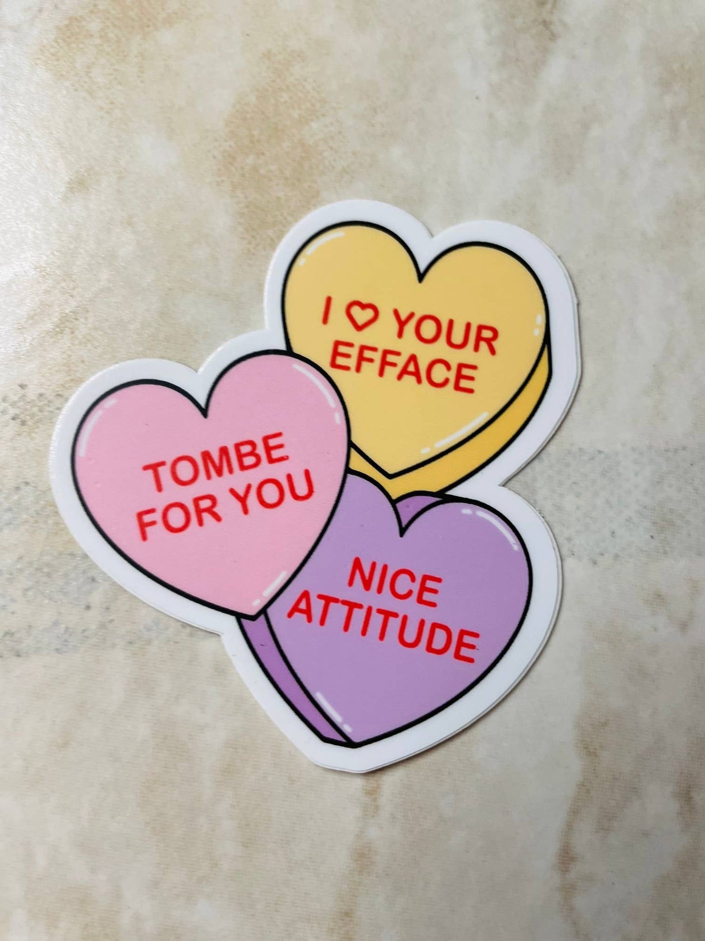 Three colorful heart-shaped stickers with humorous text on a beige surface