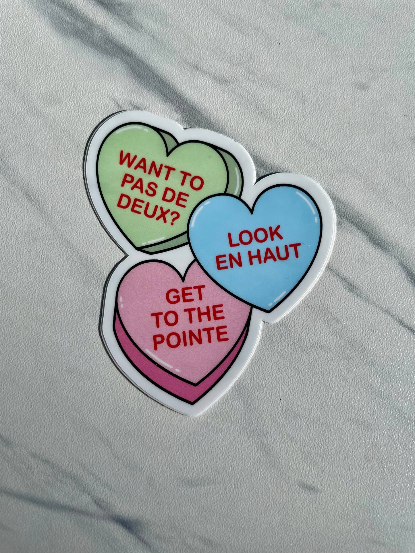 Colorful heart-shaped stickers with French dance steps on a gray fabric background