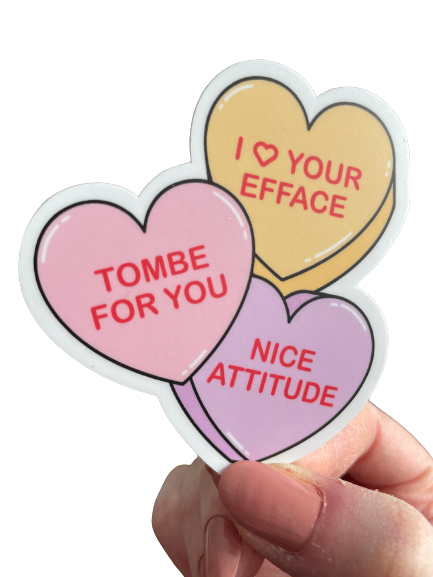 Heart-shaped stickers with humorous text held by a hand on a white background