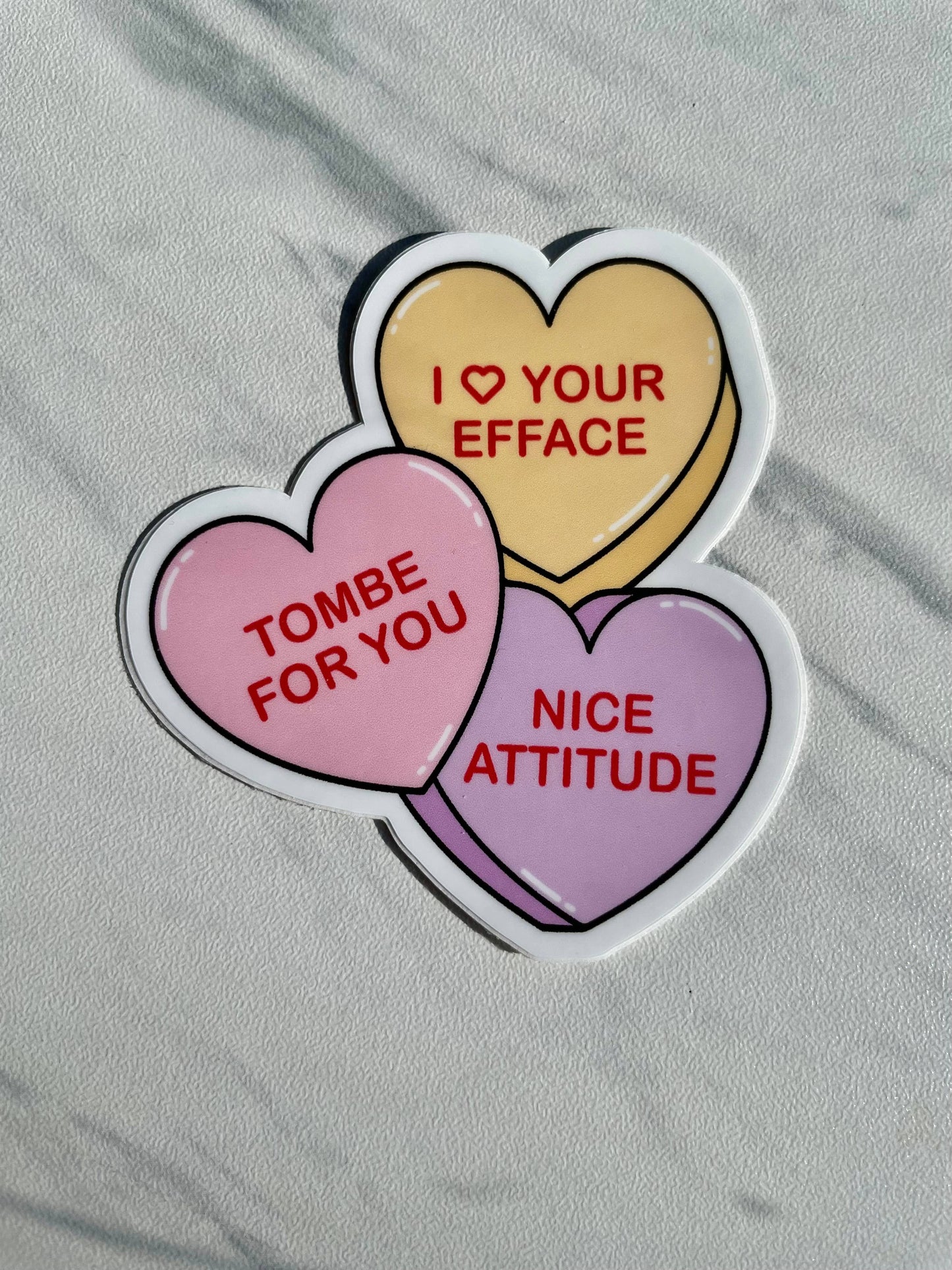 Three heart-shaped stickers with humorous text on a gray surface
