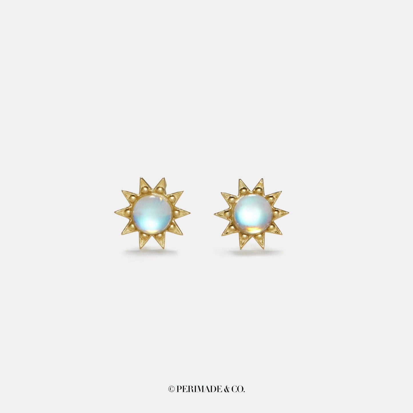 Gold sun-shaped earrings with a central gemstone on a light gray background, branded 'PERIMADE & CO'.