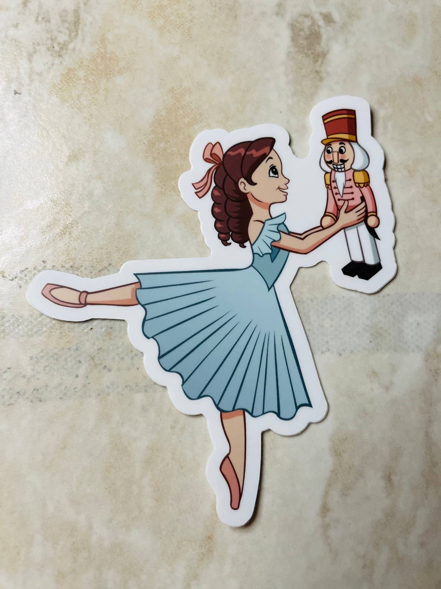 Sticker of a ballerina holding a nutcracker on a textured beige background