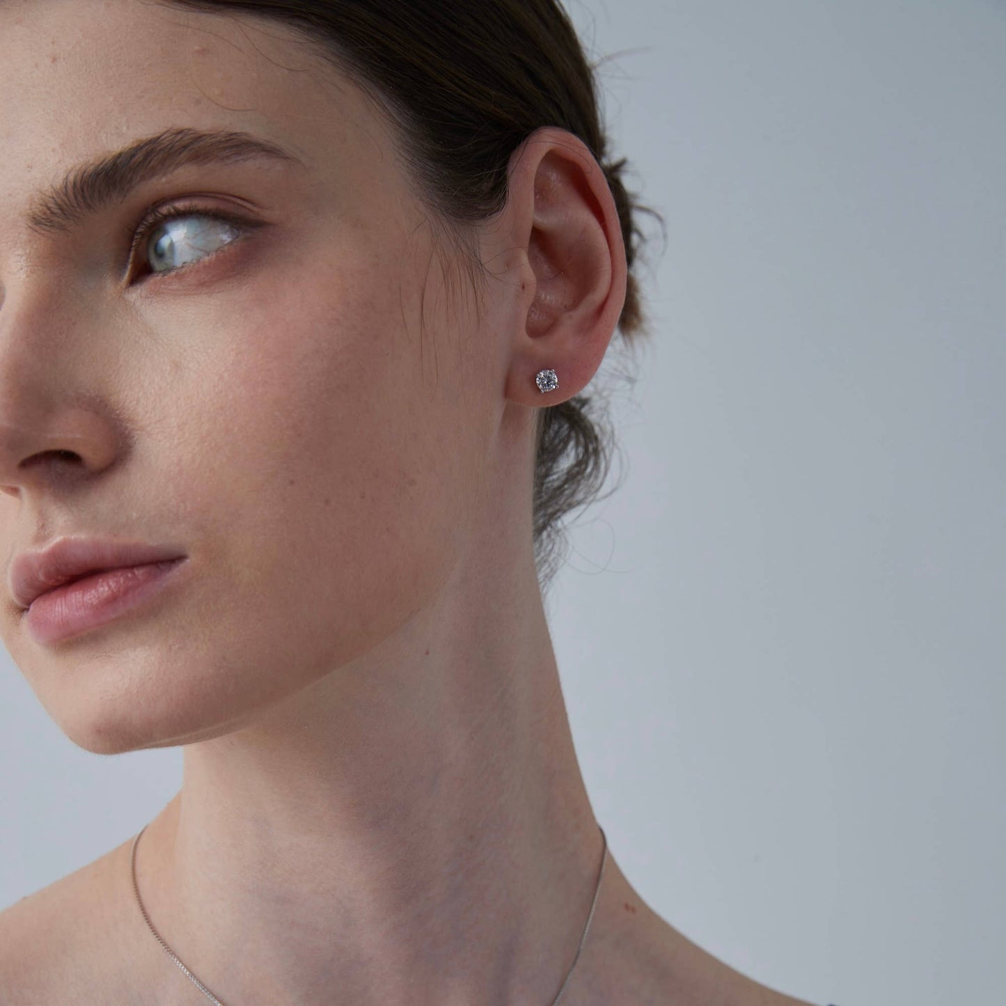 Close-up of a woman wearing a diamond earring against a plain background