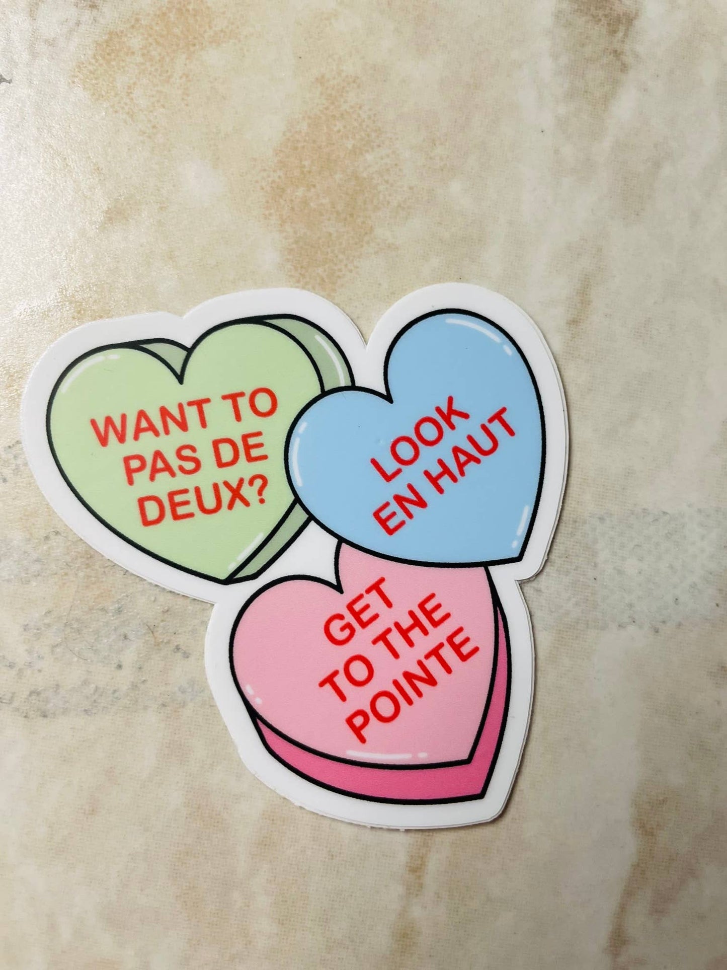 Three heart-shaped stickers with French text on a textured surface