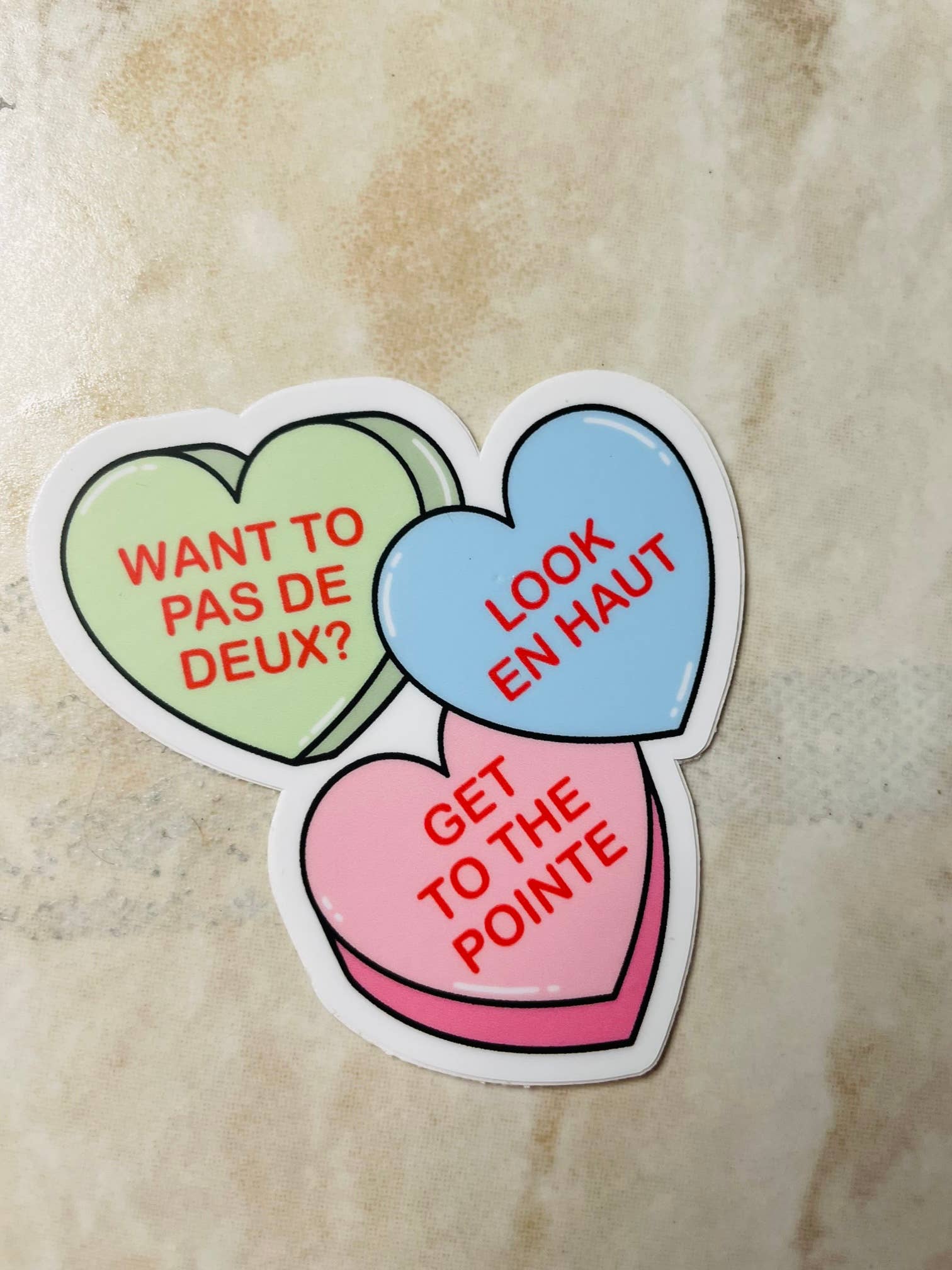 Three heart-shaped stickers with French text on a textured surface