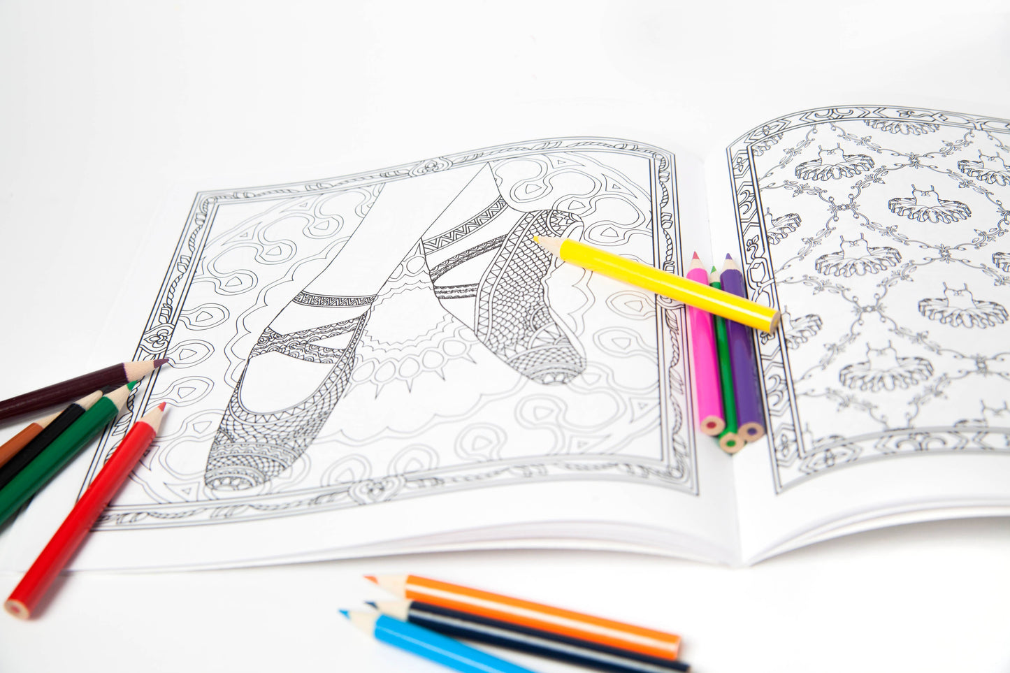 Coloring book open to pages with intricate designs and colored pencils on a white background