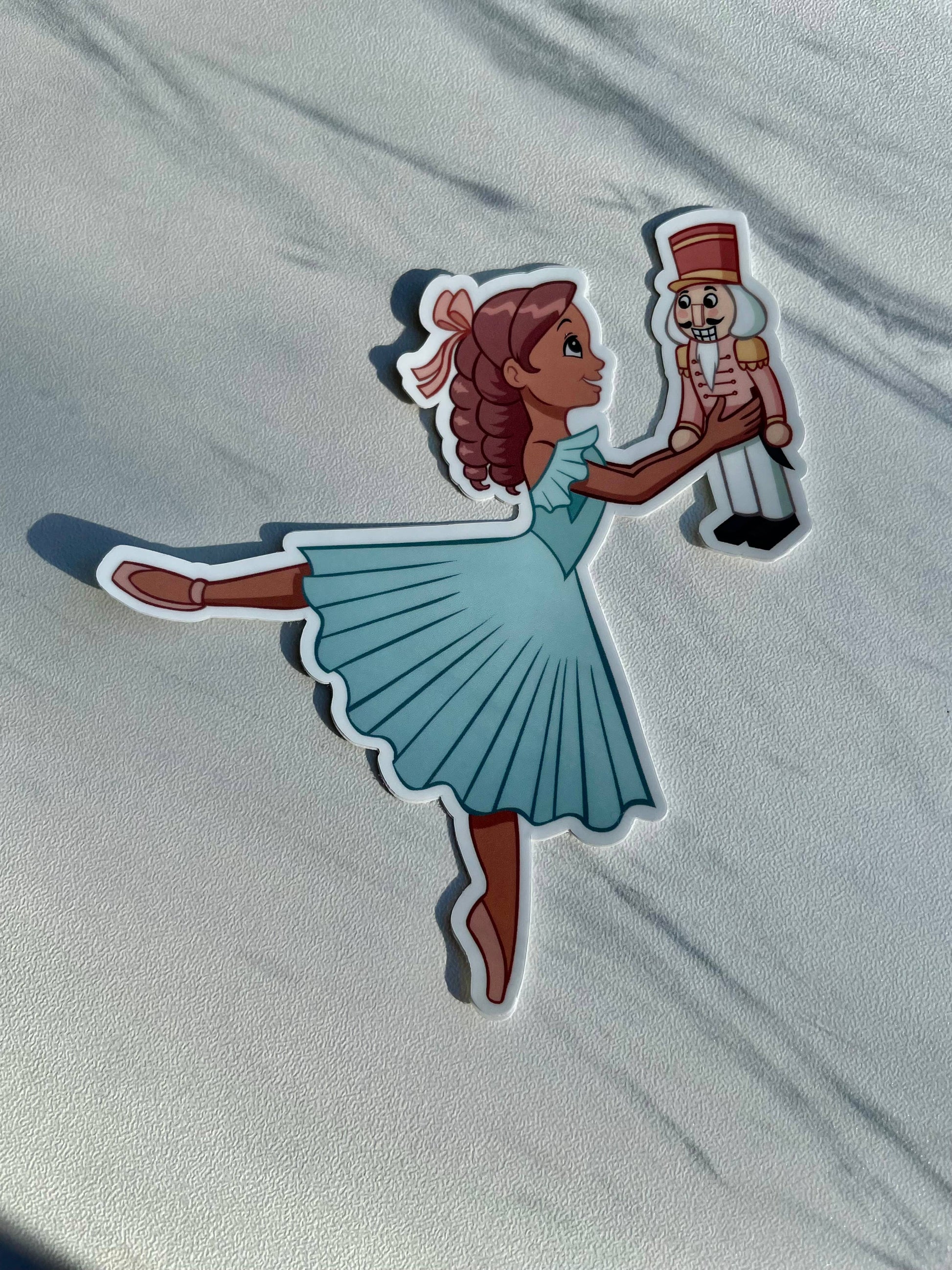 Sticker of a ballerina holding a nutcracker toy on a light gray background