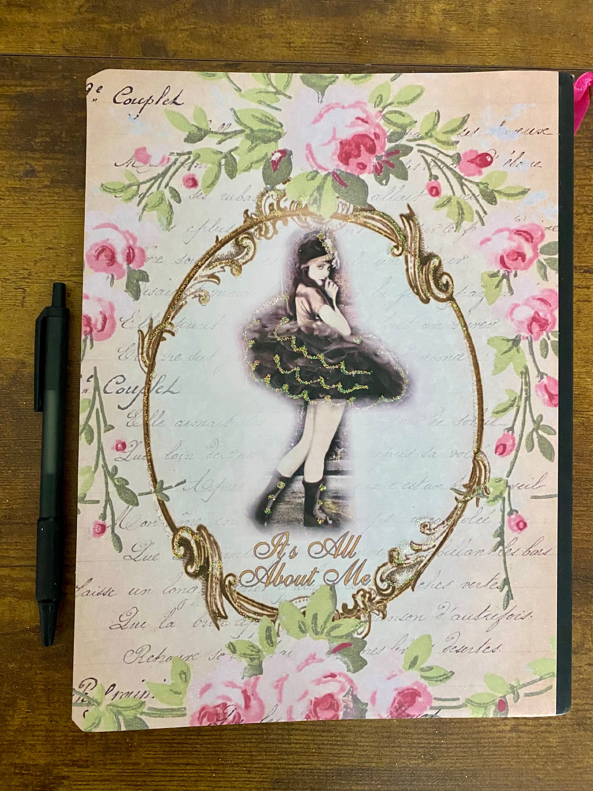 Notebook with decorative cover featuring a ballerina and floral design on a wooden surface.