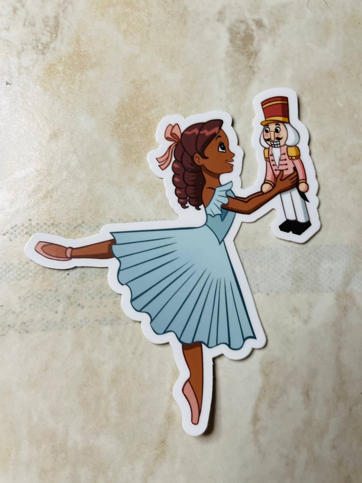 Sticker of a girl in a blue dress holding a Nutcracker toy on a textured beige background