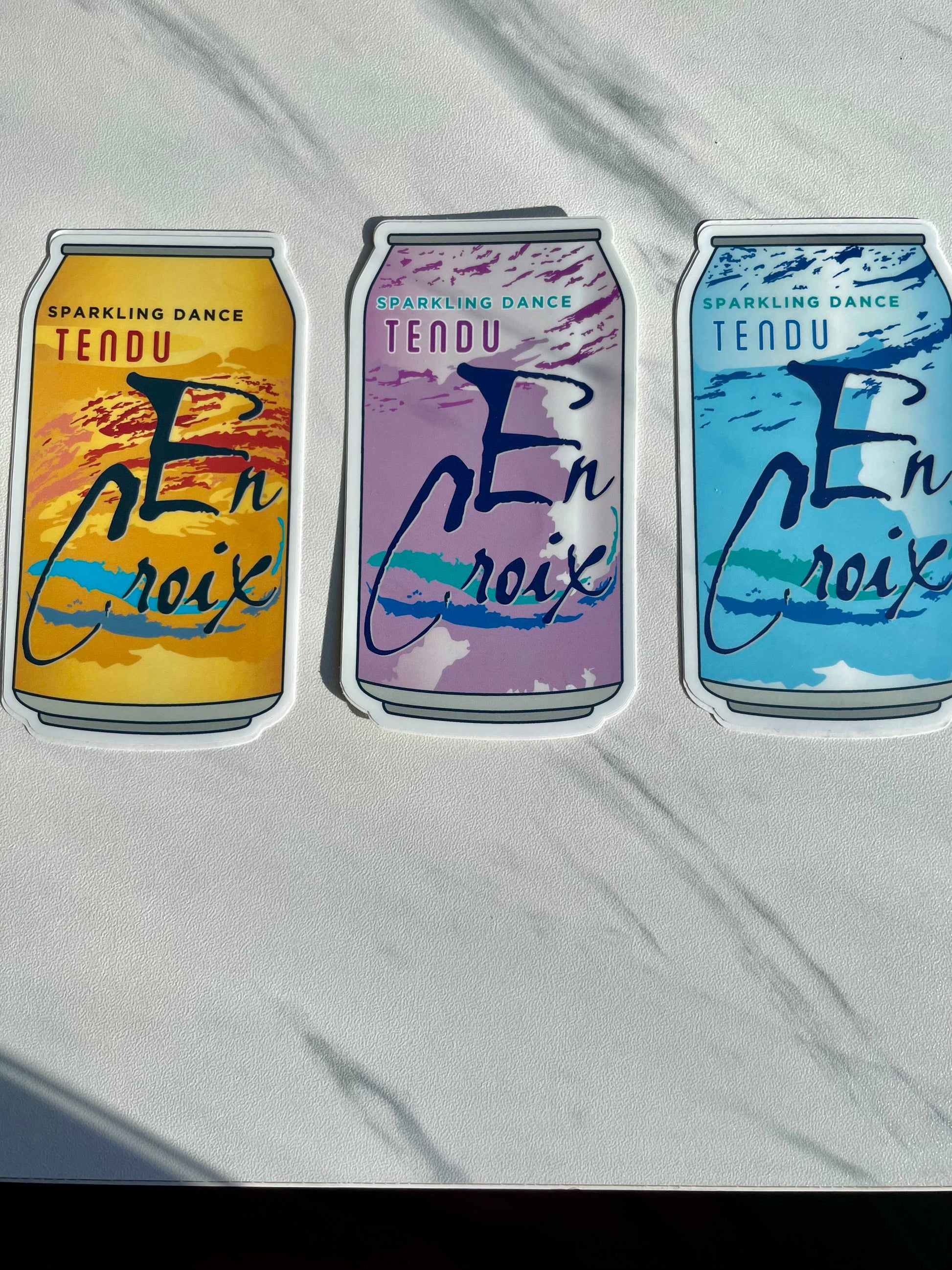 Three colorful can-shaped stickers with 'En Croix' branding on a white background.