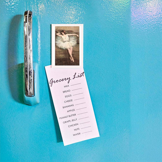 Grocery list attached to a refrigerator with a magnet, featuring a dancer illustration.