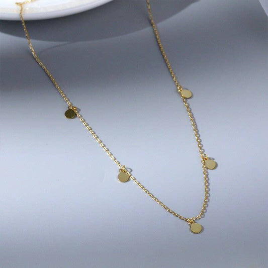Gold necklace with small round pendants on a gray background