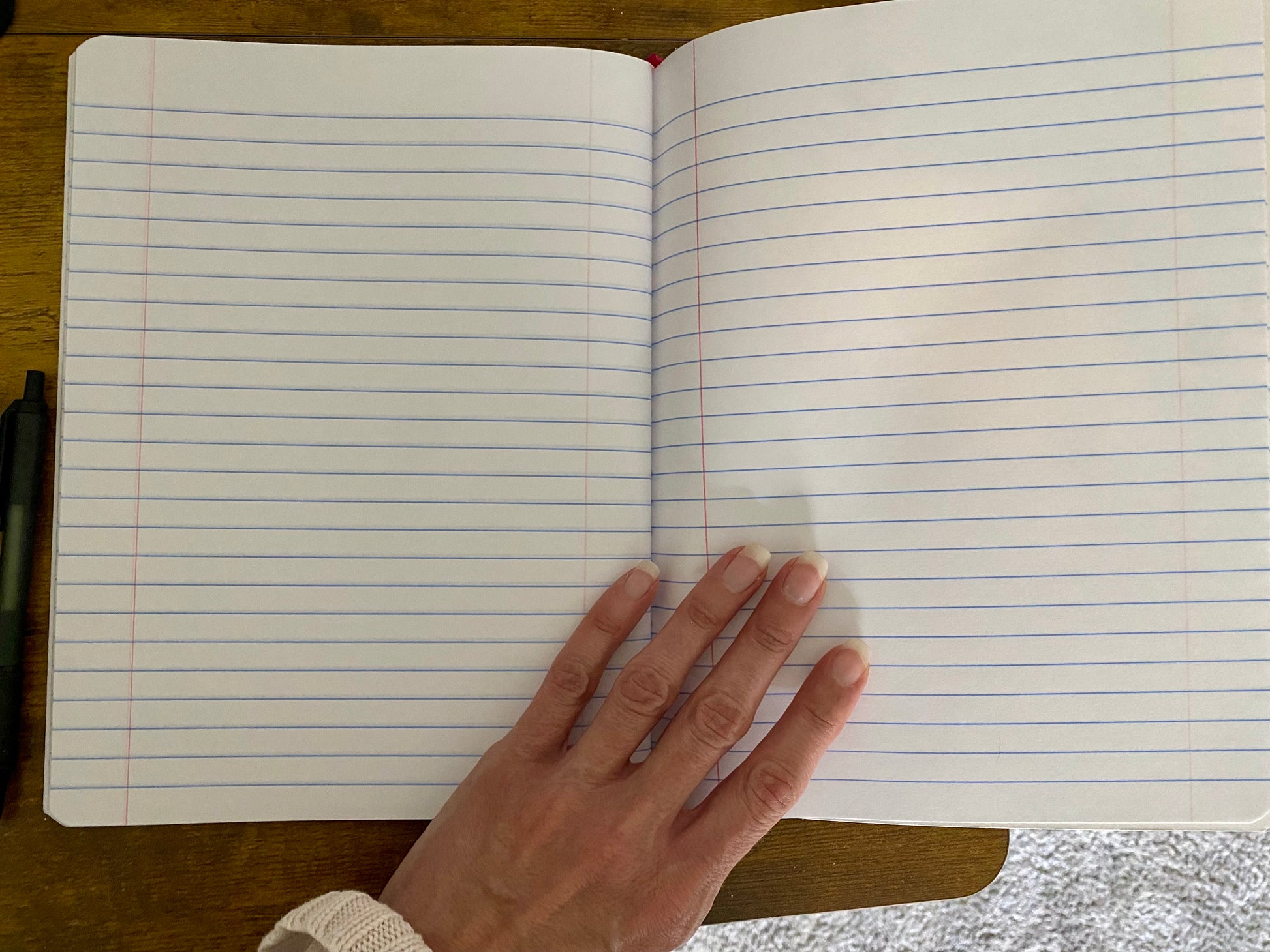 Open notebook with lined pages on a wooden surface, hand resting on top