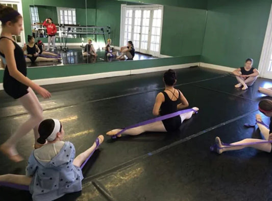 Dancers practicing with balletstrap in a studio with mirrors on the wall.