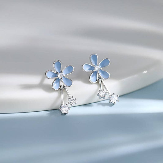 Blue flower-shaped earrings with clear stones on a light gray background