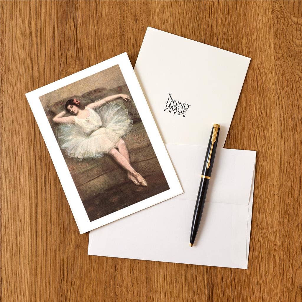Greeting card with dancer illustration, envelope, and pen on wooden surface