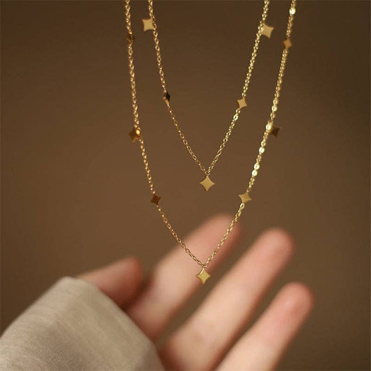 Two gold necklaces with star-shaped pendants on a hand against a brown background