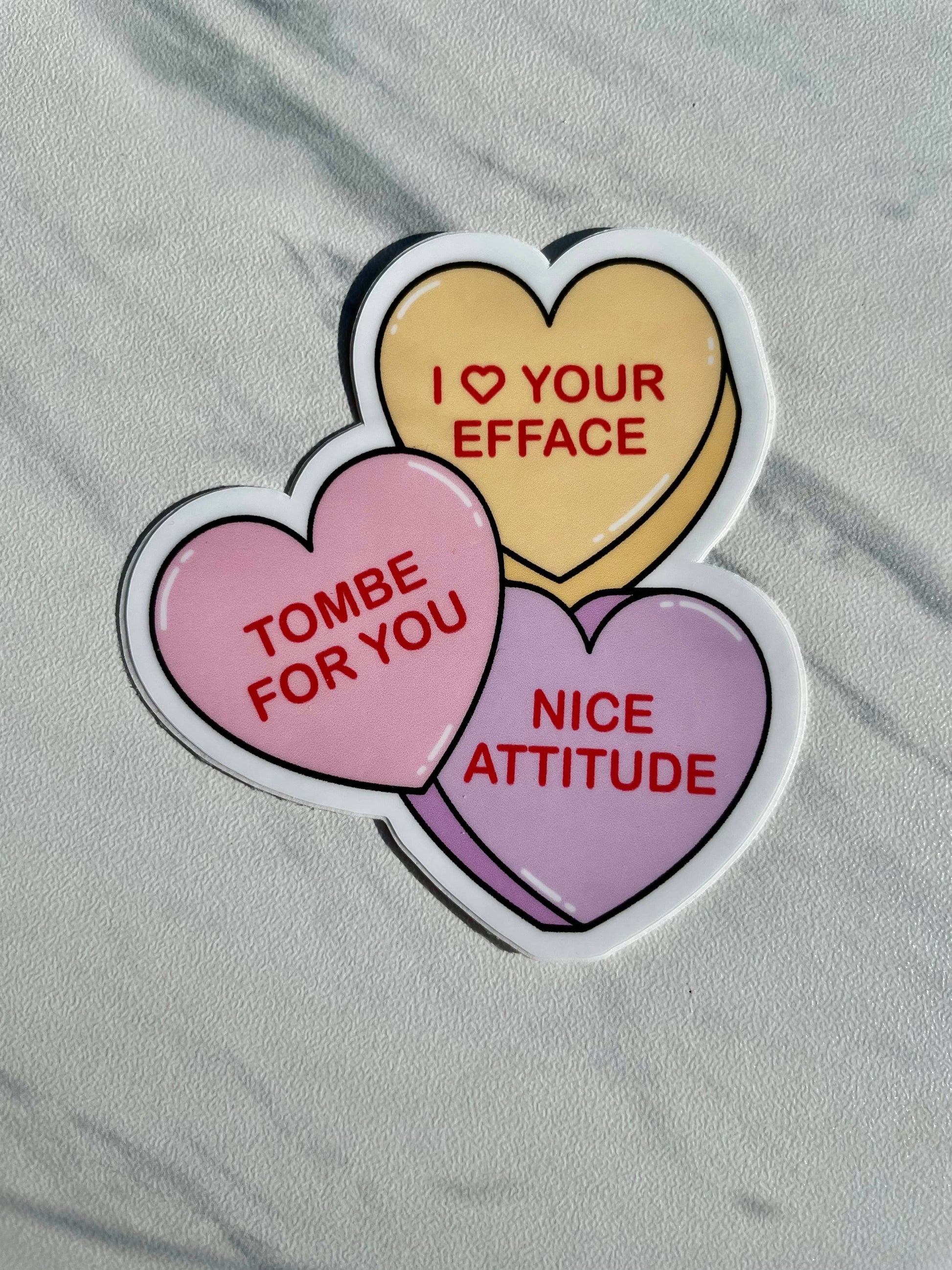 Three heart-shaped stickers with humorous text on a gray surface