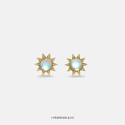 Gold sun-shaped earrings with a central gemstone on a light gray background, branded 'PERIMADE & CO'.