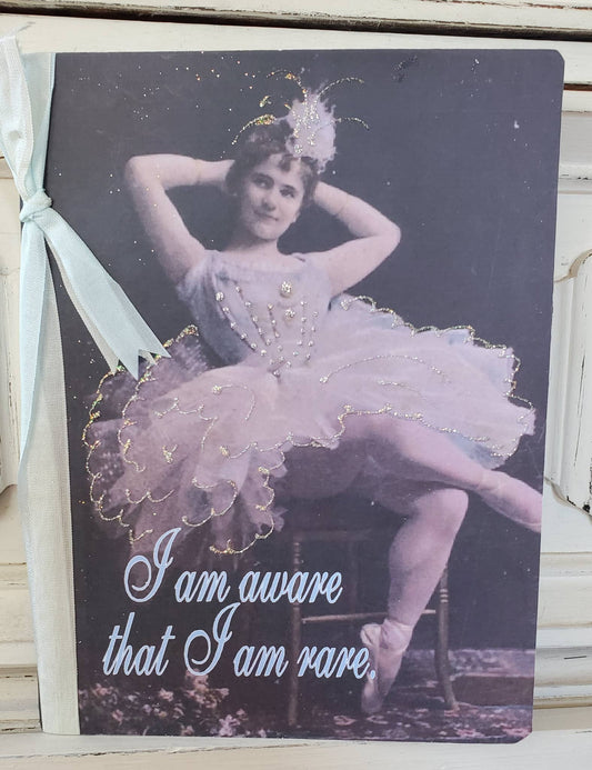 Vintage-style card with a ballerina and text 'I am aware that I am rare' on a dark background.
