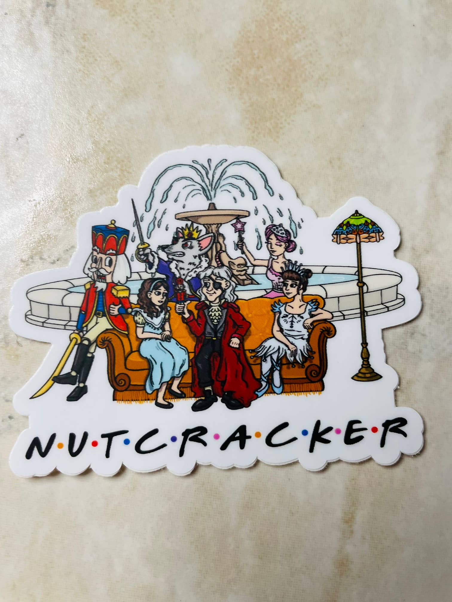 Sticker of a cartoon Nutcracker scene with characters sitting on a couch, on a beige background.
